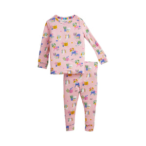 A two-piece children's pajama set featuring a long-sleeve top and matching pants in light pink, both covered in a colorful whimsical print of cats, books, and plants.